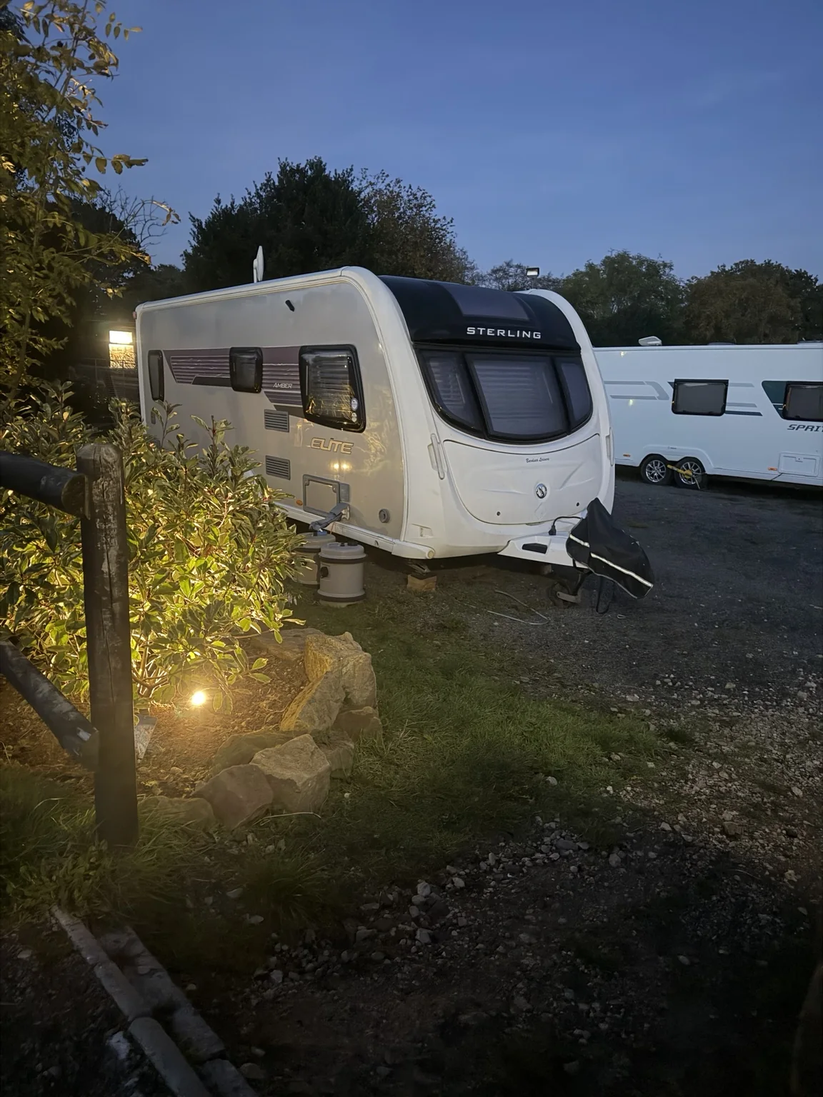 Touring caravan beside warmly illuminated planting at Glanfar Meadows in Burntwood at dusk